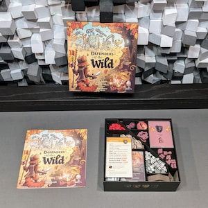 Puede incluir: Una caja de juego de mesa con un fondo marrón e ilustraciones coloridas de animales y personajes. La caja está etiquetada como "Defenders of the Wild". El juego incluye un libro de reglas, piezas de madera y cartas.