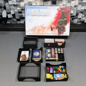 Puede incluir: Una imagen en blanco y negro de un juego de mesa llamado "Flash Point: Legacy of Flame". El juego es un emocionante juego de heroísmo y trabajo en equipo, donde cada segundo cuenta. La imagen muestra la caja del juego y varias cajas de almacenamiento de plástico negro con varios componentes del juego.
