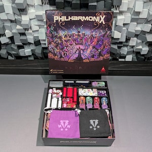 Può includere: Una scatola di gioco da tavolo intitolata "Philharmonix" con un'illustrazione colorata di musicisti. La scatola aperta rivela pezzi del gioco, tra cui miniature, dadi e sacchetti. I componenti del gioco sono ben organizzati.