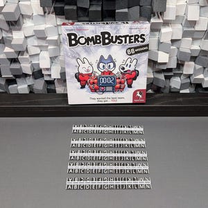 以下が含まれることがあります： 白い背景とカラフルな漫画のキャラクターが描かれたボードゲームの箱。箱には「Bomb Busters」というタイトルと「66 Missions」というテキストが書かれている。ゲームには「00:02」と表示されるタイマーが搭載されている。