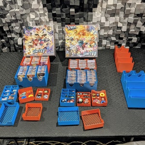 Könnte beinhalten: Ein Tischspiel-Organizer mit blauen und orangen Plastikbehältern. Die Behälter sind mit Spielkarten und Spielsteinen gefüllt. Die Spielboxen sind im Hintergrund mit dem Titel "X-Men: Marvel United" zu sehen.