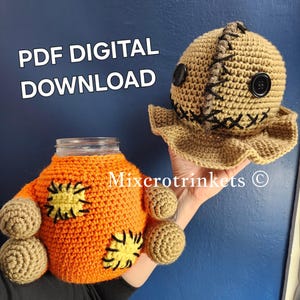 Peut inclure: Un modèle de crochet pour un couvre-jarre effrayant, orange et marron, avec un visage cousu. Le modèle est disponible en téléchargement numérique PDF. Le texte "PDF DIGITAL DOWNLOAD" est visible sur l'image.