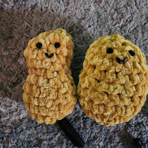 Pode incluir: Dois peluches de amendoim de cor marrom feitos de crochê com olhos pretos e rostos sorridentes.