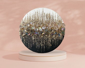 Pode incluir: Uma pintura redonda em tela preta e dourada com uma superfície texturizada. A pintura apresenta um desenho de cristais iridescentes e glitter dourado.