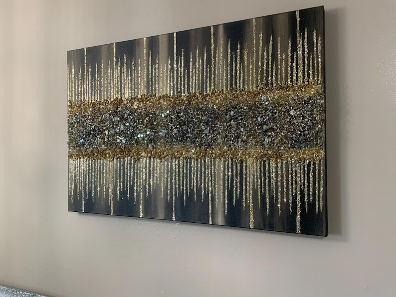 Puede incluir: Una pintura rectangular sobre lienzo con un dise&ntilde;o abstracto texturizado. La pintura presenta un fondo oscuro con l&iacute;neas verticales de purpurina dorada y una banda horizontal de purpurina dorada y plateada.