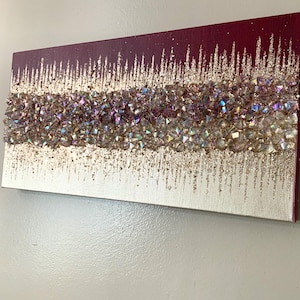 May include: Abstract canvas art with a gradient of silver, gold, and burgundy. The artwork features a textured band of iridescent crystals. The design includes vertical gold glitter accents, creating a shimmering effect. This piece is suitable for home decor.