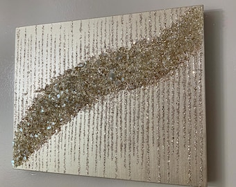 May include: A gold and silver glitter canvas wall art with a diagonal line of iridescent glitter. The glitter is arranged in a random pattern, creating a textured effect.