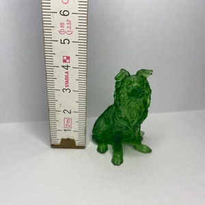 Könnte beinhalten: Eine grüne Glasfigur eines sitzenden Hundes mit aufgestellte Ohren. Die Figur ist etwa 5 cm hoch.
