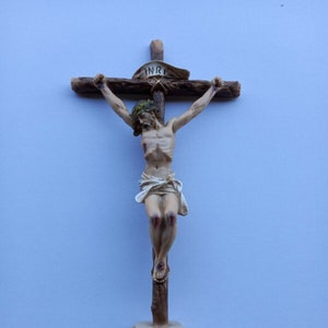 May include: A wooden crucifix with a sculpted figure of Jesus Christ on the cross. The figure is painted in a realistic style with details of wounds and blood. The cross is mounted on a base that resembles a rocky hill.