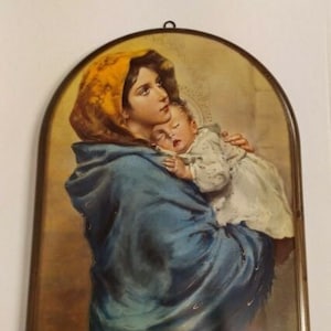 May include: A vintage religious painting depicting a mother and child. The mother is wearing a blue robe and a yellow head covering. The child is asleep in her arms. The painting is framed in a wooden frame.