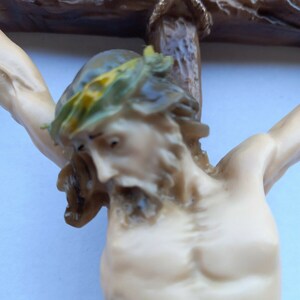 May include: A close-up of a religious figurine depicting a person on a wooden cross. The person has a crown of thorns and a red wound on their side. The cross is made of brown wood and has a gold inscription.