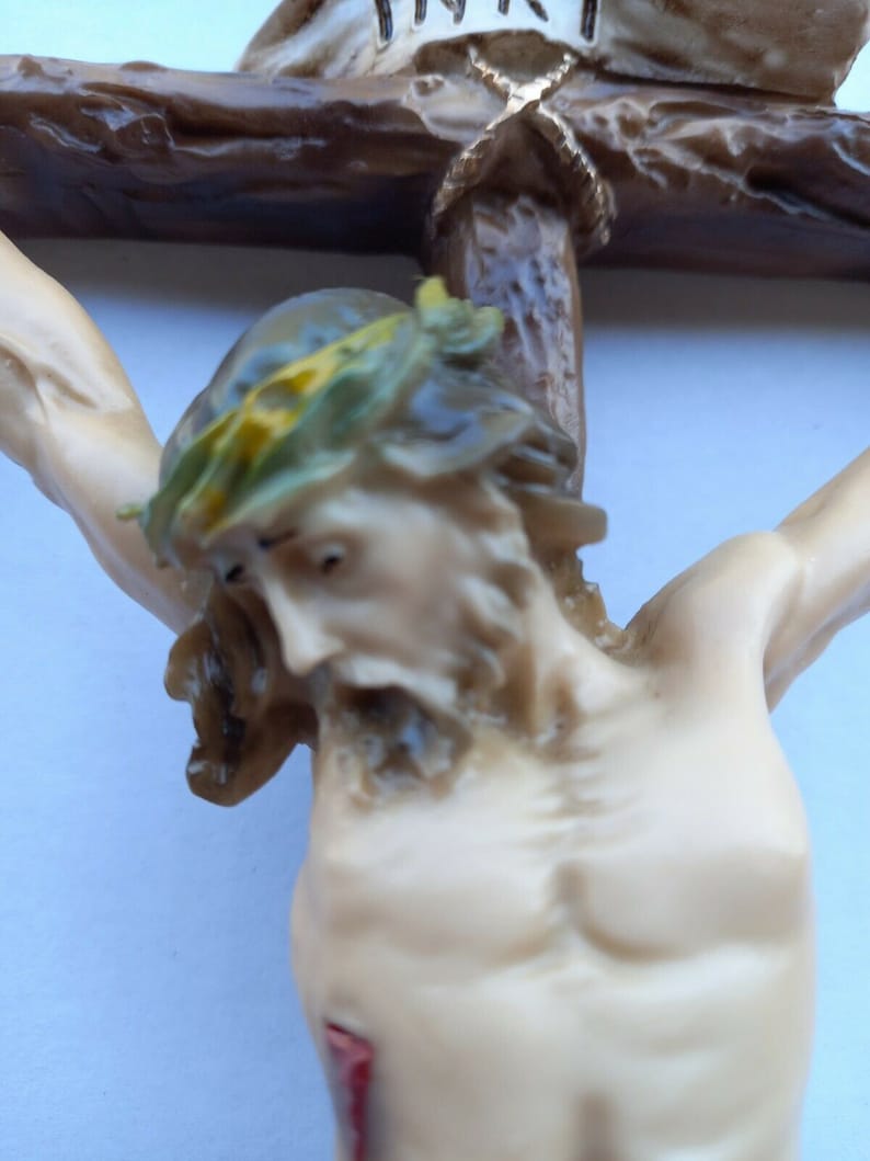 May include: A close-up of a religious figurine depicting a person on a wooden cross. The person has a crown of thorns and a red wound on their side. The cross is made of brown wood and has a gold inscription.
