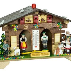 May include: A wooden Heidi Haus weather station with a thermometer, figurines, and a dog. The house has a gray roof, red accents, and a green base. The text "HEIDI HAUS" is visible on the base.