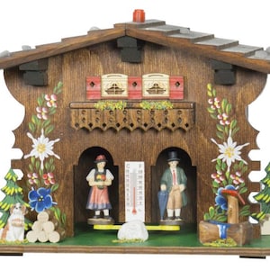 May include: A wooden chalet-style decorative piece with a pitched roof, featuring painted floral accents and miniature figures. The chalet has two arched openings with figurines, a thermometer, and a small water fountain.