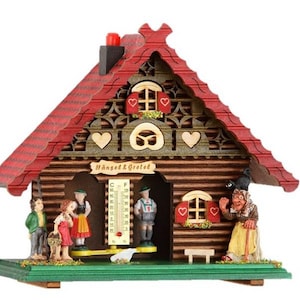 May include: A decorative wooden cuckoo clock shaped like a house with a red roof. The clock features miniature figures of children and a witch, with the text "Hänsel & Gretel" above the entrance. The clock has a green base and a thermometer.