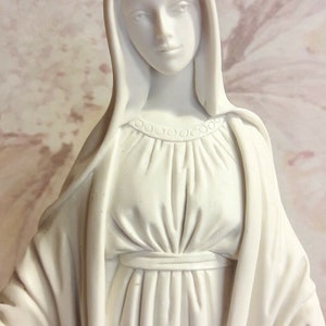 Puede incluir: Estatua de yeso blanco de la Virgen Mar&iacute;a, con una larga t&uacute;nica y un velo. La estatua tiene una expresi&oacute;n serena en su rostro.