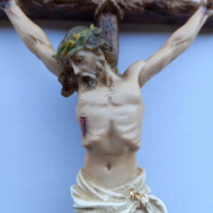 May include: A white figurine of a person on a wooden cross with the word "INRI" above. The person is wearing a crown of thorns and has a cloth draped around their waist.