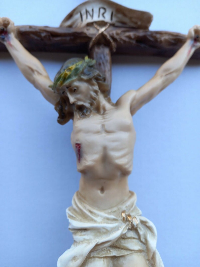May include: A white figurine of a person on a wooden cross with the word "INRI" above. The person is wearing a crown of thorns and has a cloth draped around their waist.