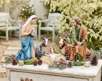 May include: A Nativity scene with figurines of Mary, Joseph, baby Jesus, a donkey, and a cow. The figures are on a white dresser, decorated with pinecones, berries, and greenery. The figures are painted in muted colors.