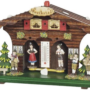 May include: A wooden Musikstadt weather house with miniature figures in traditional Bavarian attire. The house features a thermometer, decorative trim, and a sign that reads "Musikstadt". The figures include musicians and dancers.
