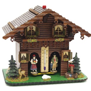 May include: A wooden cuckoo clock in the shape of a chalet. The clock features miniature figures, a thermometer, and decorative elements like trees and a deer. The roof is gray, and the clock has a green base.
