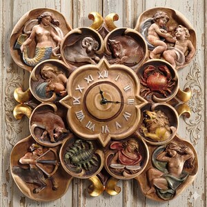 May include: A decorative wall clock featuring zodiac signs and Roman numerals. The clock has a central face with a starburst design and is surrounded by sculpted figures representing the zodiac. The clock is made of a light brown material with gold accents.