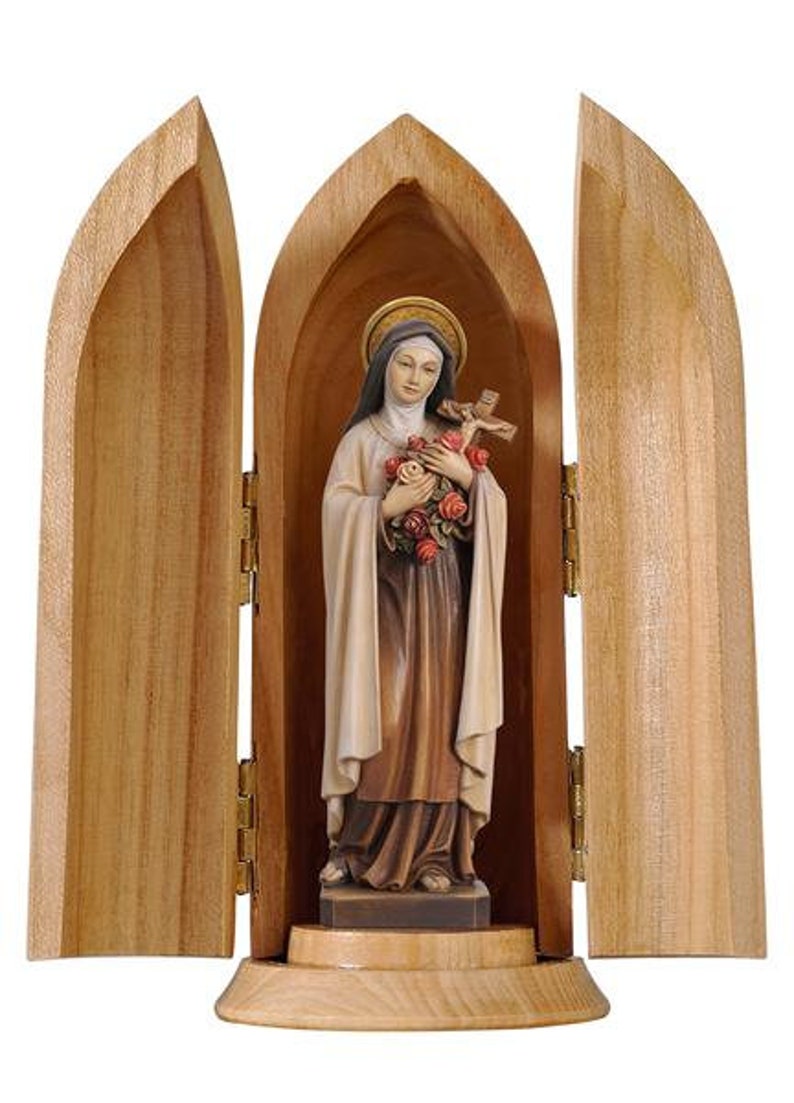 May include: A wooden shrine with a hinged door, revealing a statue of a woman holding a bouquet of roses and a cross. The statue is painted in shades of white, brown, and pink.