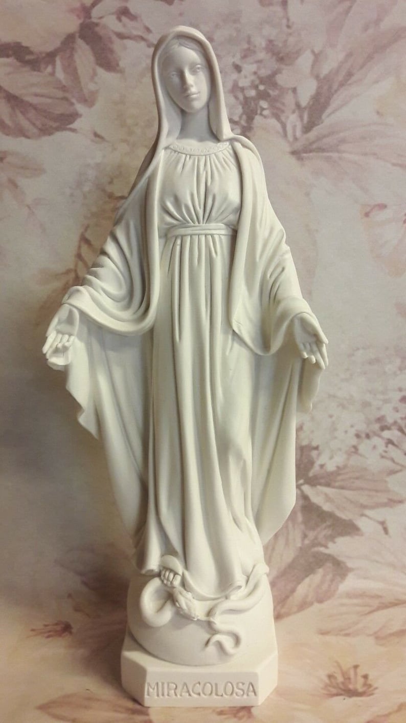 Puede incluir: Estatua blanca de la Virgen Mar&iacute;a, de pie con los brazos extendidos, vestida con una larga t&uacute;nica y un velo. La estatua est&aacute; sobre una base con la palabra "MIRACOLOSA" inscrita en ella.