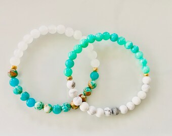 May include: Two beaded bracelets with a gradient of turquoise and white beads. The bracelets are made with natural stones and gold accents.