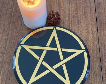 May include: A black circular altar plate with a gold pentagram design. The plate is on a wooden surface.