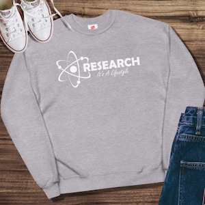 以下が含まれることがあります： 白い原子記号と「RESEARCH It's A Lifestyle」というテキストが書かれた灰色のスウェットシャツです。