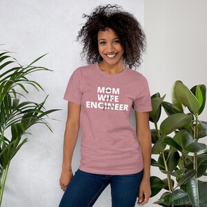 May include: A heather pink t-shirt with the text "MOM wife ENGINEER" in black lettering.