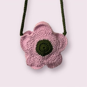 May include: A pink crocheted flower-shaped bag with a green crocheted center. The bag has a green crocheted strap.