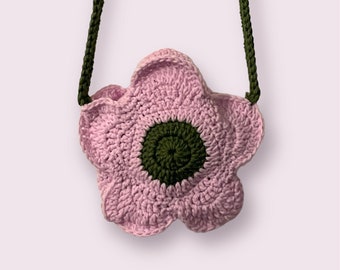 May include: A pink crocheted flower-shaped bag with a green crocheted center. The bag has a green crocheted strap.