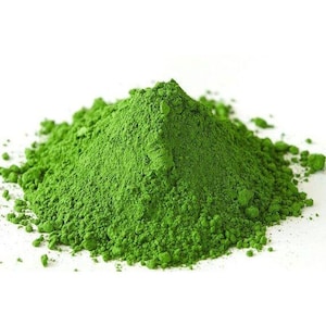 Könnte beinhalten: Ein Haufen fein gemahlenes Matcha-Pulver, das einen leuchtenden Grünton aufweist. Das Pulver hat eine feine, fast flauschige Textur mit einer unebenen Oberfläche. Die Farbe ist ein sattes, grünes Grün, das Frische und Qualität suggeriert. Das Bild ist vor einem sauberen weißen Hintergrund.