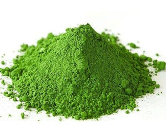 May include: A vibrant pile of finely ground, bright green matcha powder. The powder has a fine, almost fluffy texture, with a slightly uneven surface. The color is a rich, verdant green, suggesting freshness and quality. The image is set against a clean white background.
