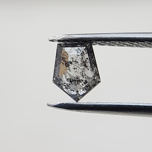 May include: A gray, faceted, hexagonal diamond with black inclusions held by tweezers.