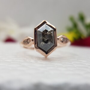 May include: A rose gold ring with a hexagonal shaped black diamond and smaller diamonds on the band.