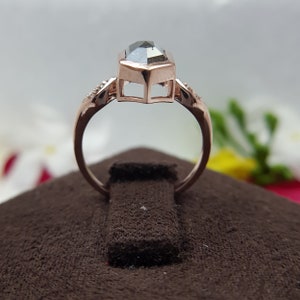 May include: A rose gold ring with a large, dark gray, octagon-shaped gemstone. The ring is set with smaller diamonds on the band.