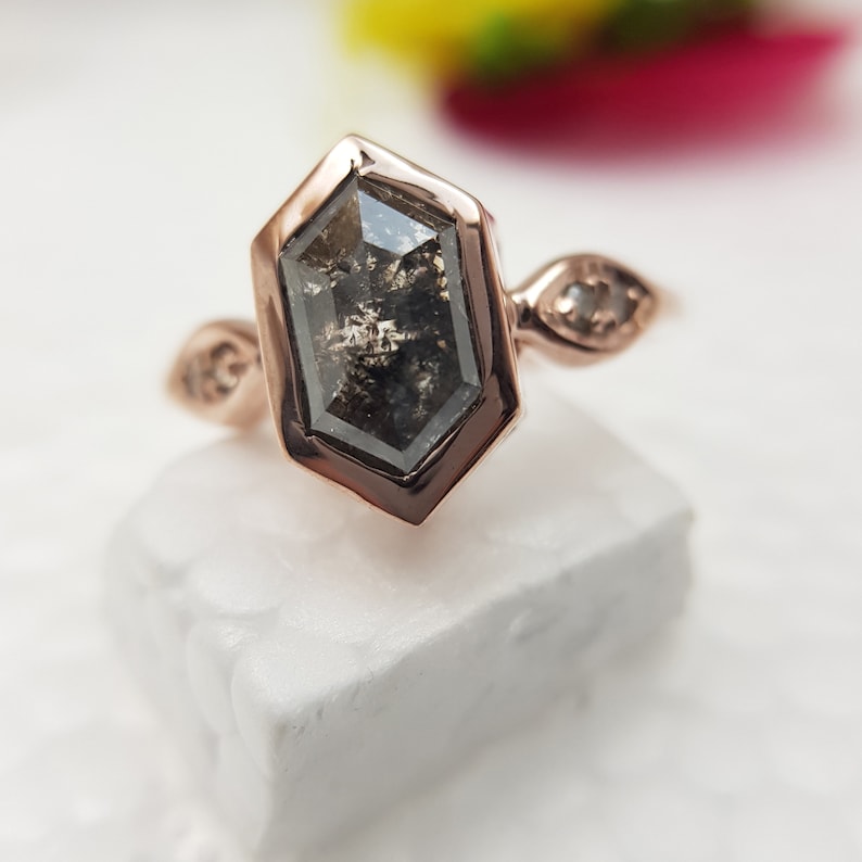 May include: A rose gold engagement ring with a hexagonal black diamond and two smaller diamonds on the band.