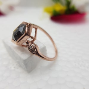May include: A rose gold ring with a large, hexagonal, black diamond and two smaller diamonds on the band.