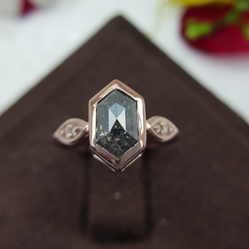 May include: A rose gold engagement ring with a hexagonal black diamond and two smaller diamonds on the band.