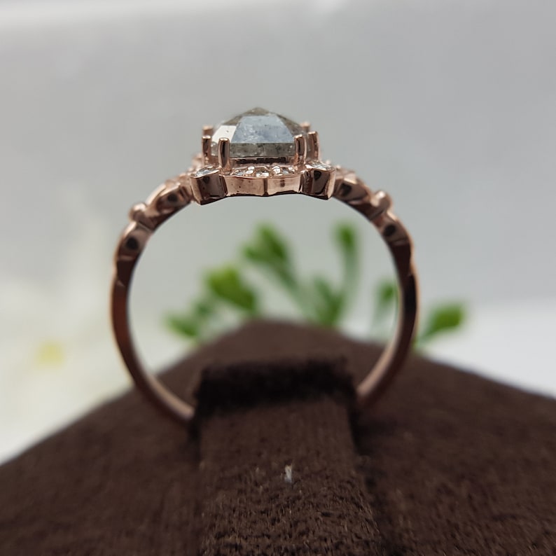 May include: A rose gold engagement ring with a gray, pear-shaped diamond set in a delicate floral halo. The ring is on a brown velvet surface.
