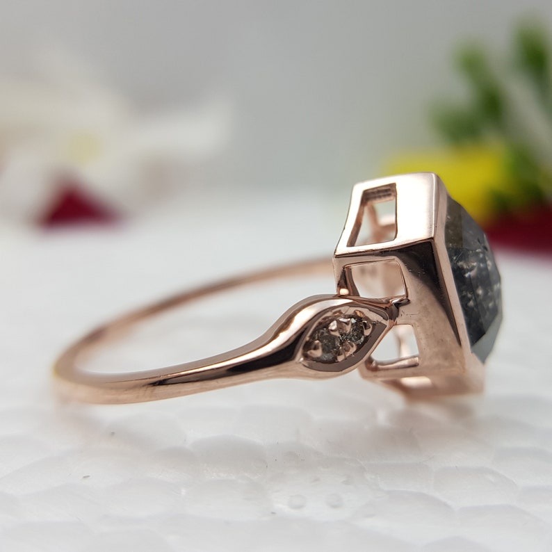 May include: A rose gold engagement ring with a square-shaped black diamond and two smaller diamonds on the band.