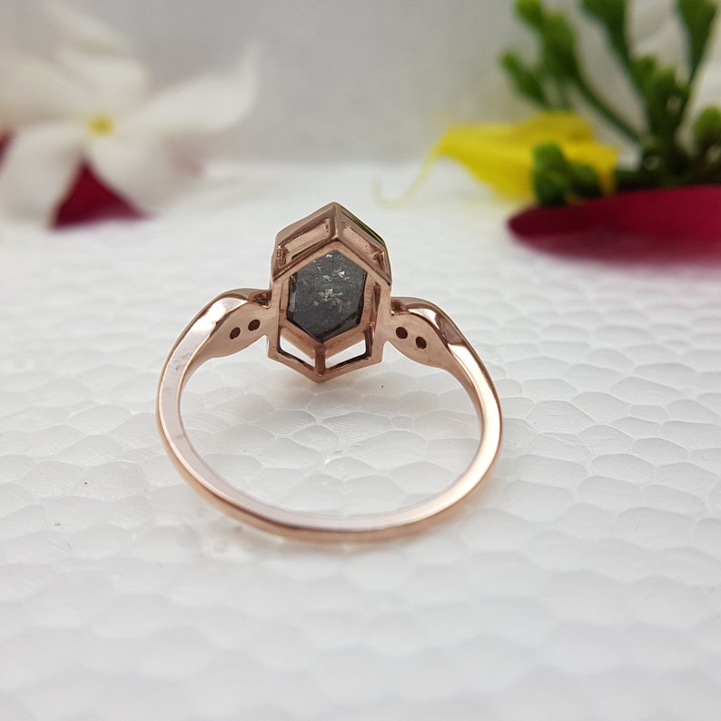 May include: A rose gold ring with a hexagonal setting featuring a grey diamond. The ring has two small diamonds on each side of the main stone.