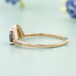 May include: A delicate gold ring with a black pear-shaped gemstone surrounded by a halo of smaller diamonds.