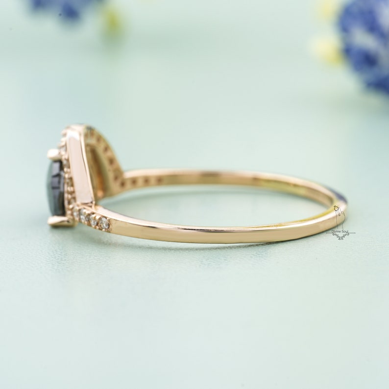 May include: A delicate gold ring with a black pear-shaped gemstone surrounded by a halo of smaller diamonds.