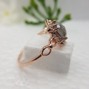 May include: A rose gold ring with a large, clear, faceted gemstone set in a delicate, ornate setting. The ring has a delicate band with a chain-like design.