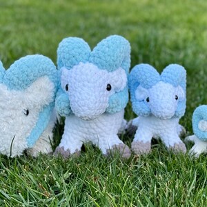 May include: Four plush toys in varying sizes, arranged on green grass. The toys are white with light blue accents and feature a stylized animal design. The largest toy is approximately 12 inches tall, with the smallest being about 4 inches.