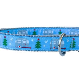 May include: A blue dog collar with a festive pattern of silver camper vans, green Christmas trees, and snowflakes. The collar has a silver metal D-ring.